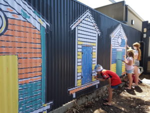 children painting colourful beach hunts on a fence